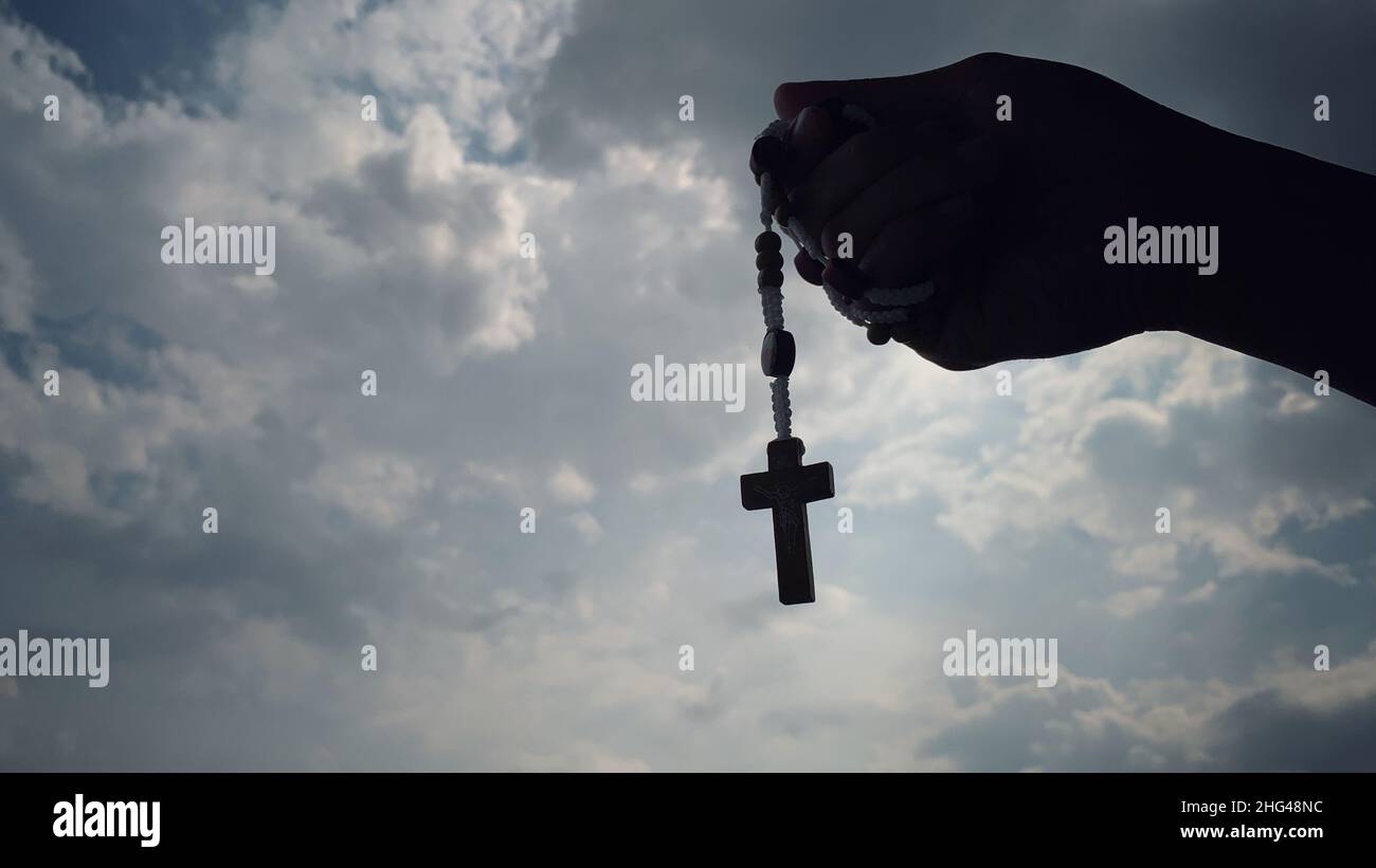 Concept religieux chrétien de la main tenant un Saint Rosaire avec fond de ciel. Banque D'Images