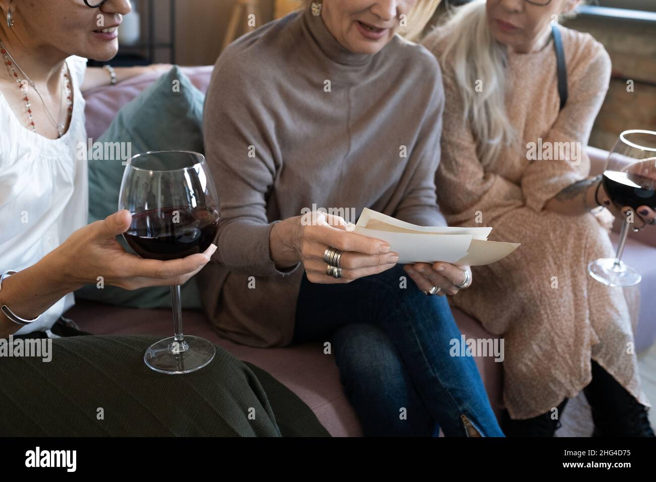 Gros plan d'une femme mûre assise sur un canapé en regardant des photos avec ses amis pendant qu'ils boivent du vin rouge Banque D'Images