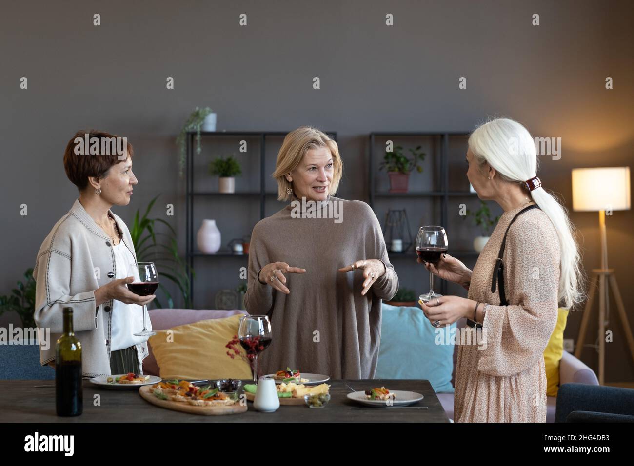 Groupe de femmes matures discutant entre elles et buvant du vin rouge pendant le dîner à la maison Banque D'Images