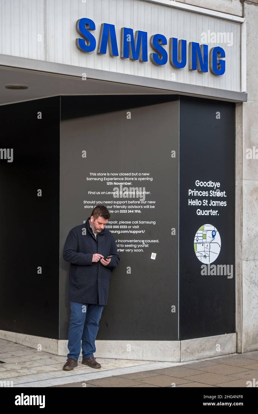 Homme utilisant un téléphone mobile à l'entrée du magasin Samsung fermé sur Princes Street, ayant déménagé dans le nouveau quartier St James, Edimbourg, Écosse, Royaume-Uni. Banque D'Images