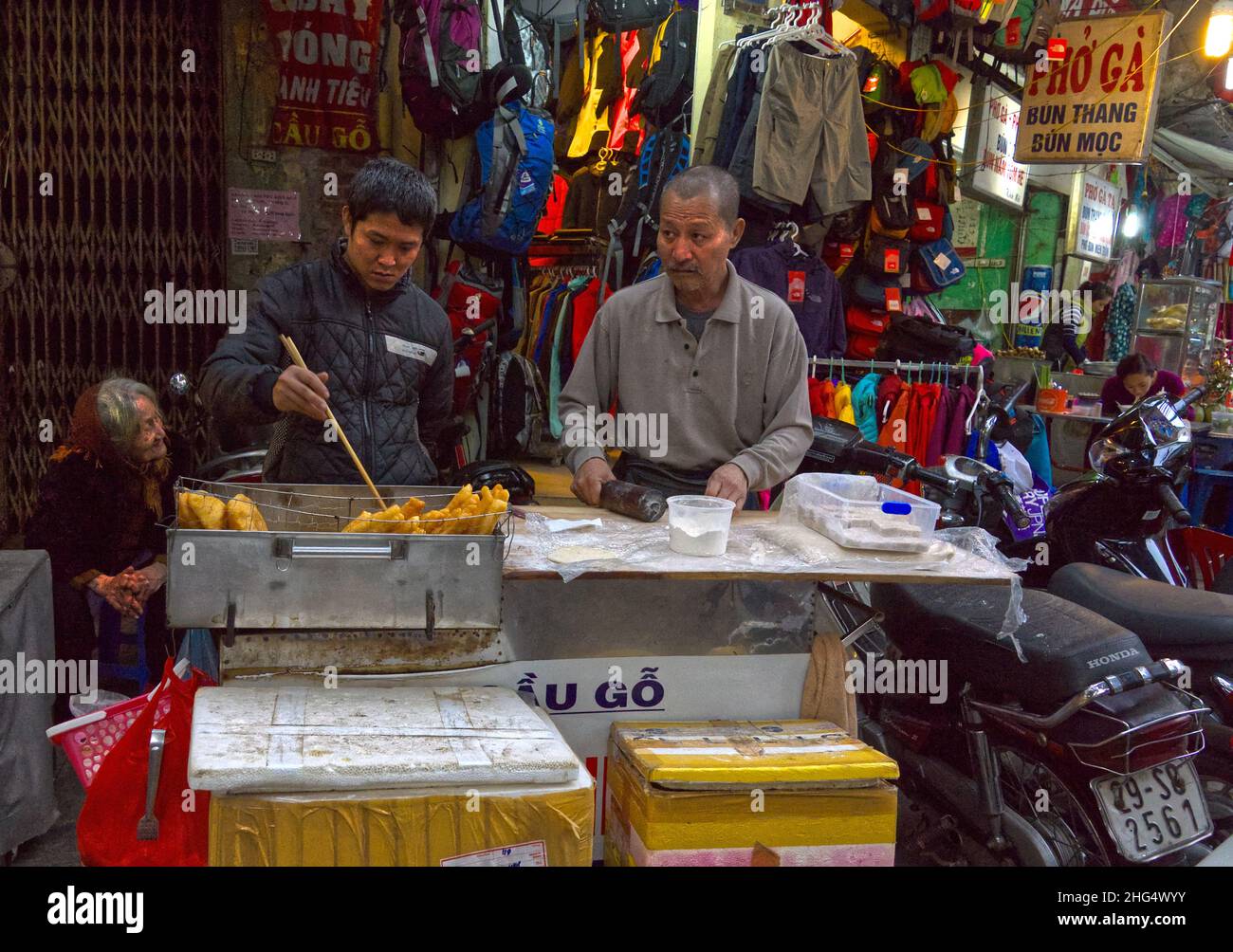 Ein vietnamesisches Paar verkauft abends auf der Straße frittierte Backwaren in einer typischen situation - die Oma sitzt in der Ecke und schaut zu Banque D'Images