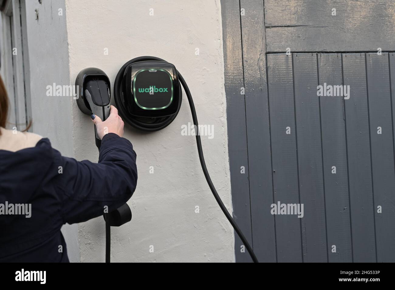 Personne qui remplace un chargeur de voiture électrique EV sur la prise murale d'un garage Banque D'Images