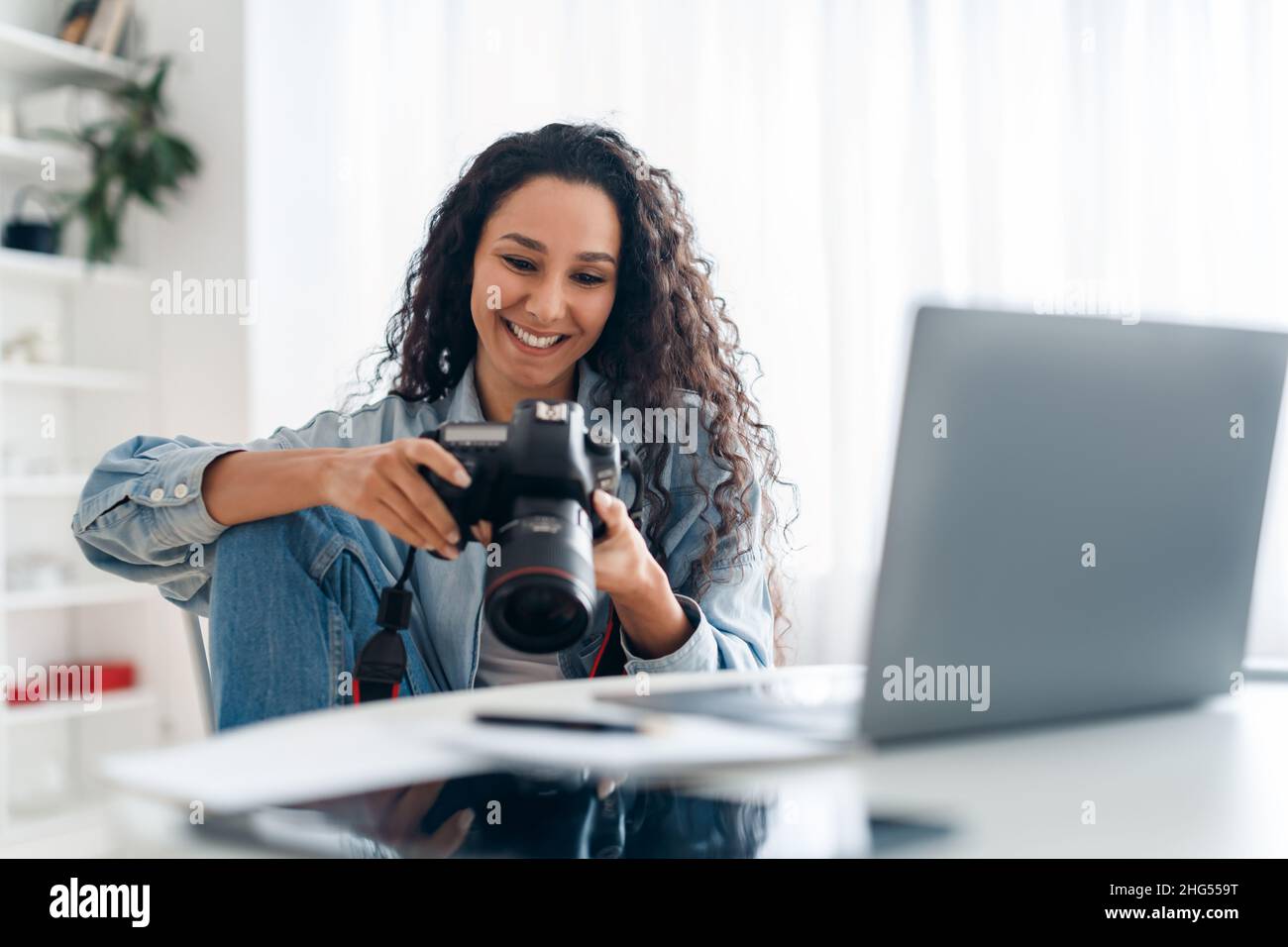 Photographe féminine tenant un appareil photo regardant des photos à l'intérieur d'un ordinateur portable Banque D'Images