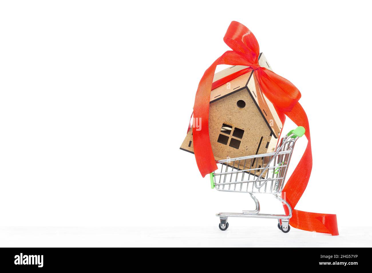 Modèle de maison miniature décoré d'un noeud de ruban rouge dans un petit chariot isolé sur blanc.Achat de biens en ligne. Banque D'Images