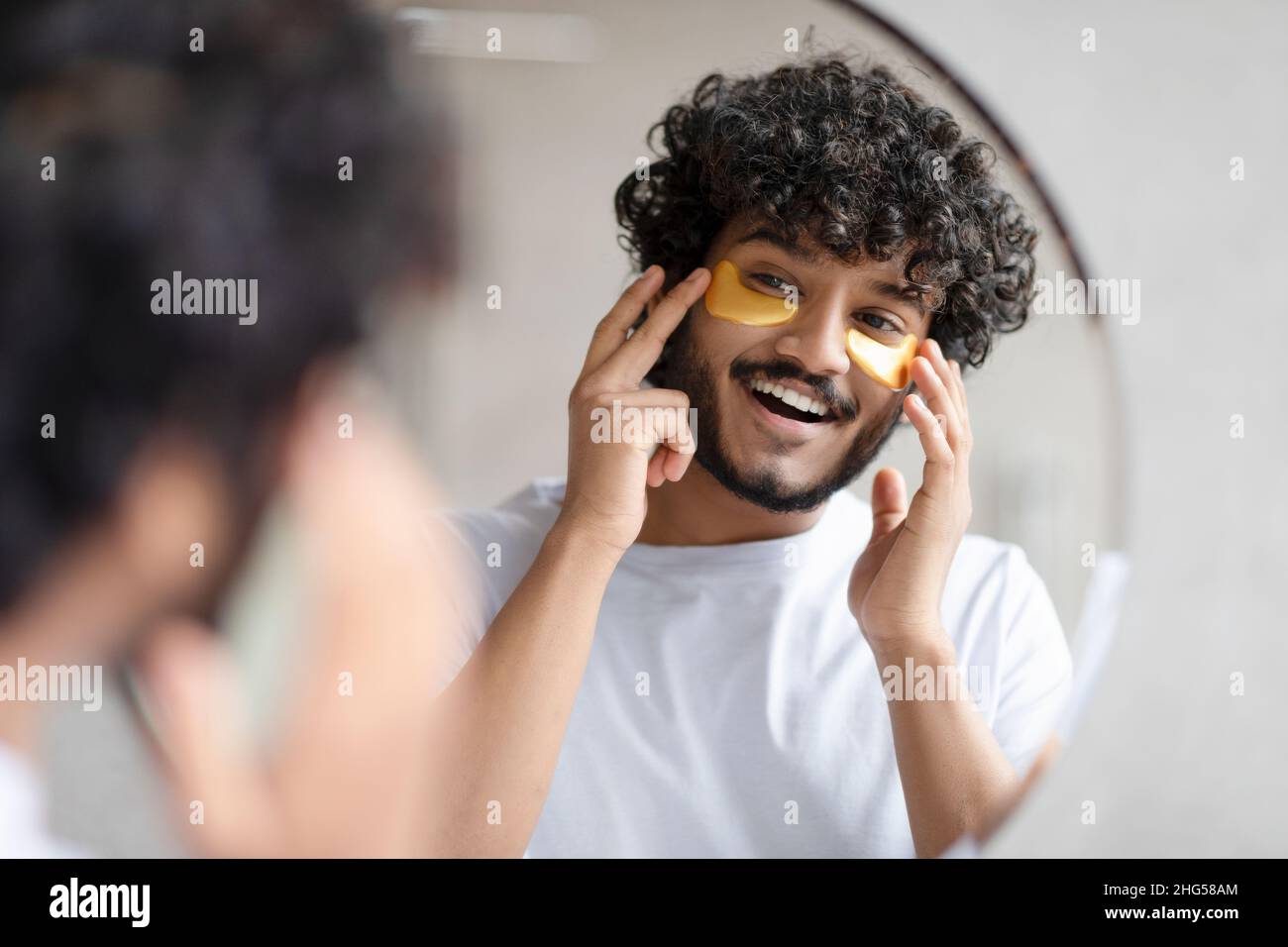 Portrait d'un indien appliquant des cellules oculaires sur son visage et regardant le miroir à la salle de bains Banque D'Images