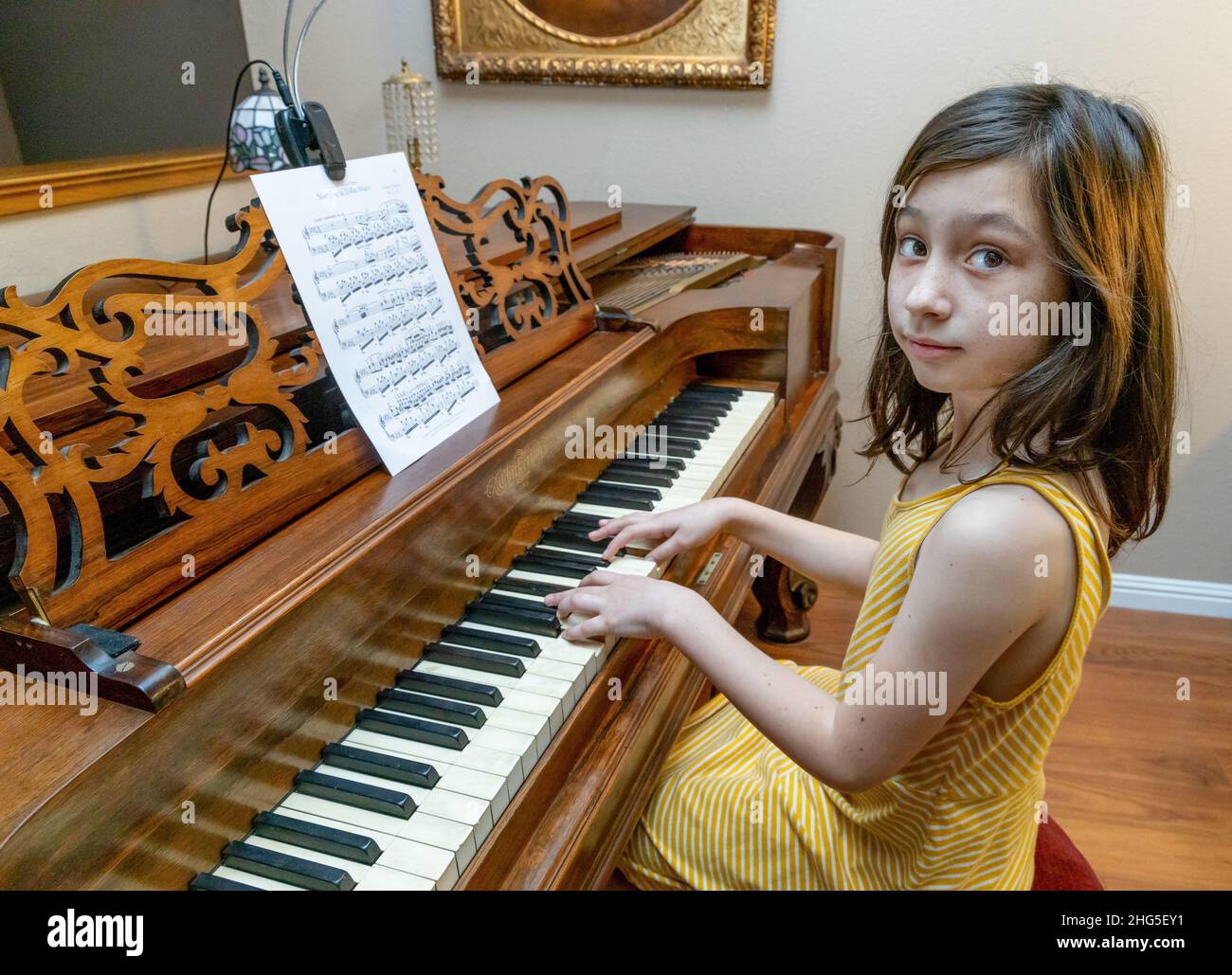 Une jeune fille vêtu d'une robe jaune jouant un rare piano antique Chilling & Sons Square Grand construit en 1867 avec une peinture antique dans un cadre doré. Banque D'Images