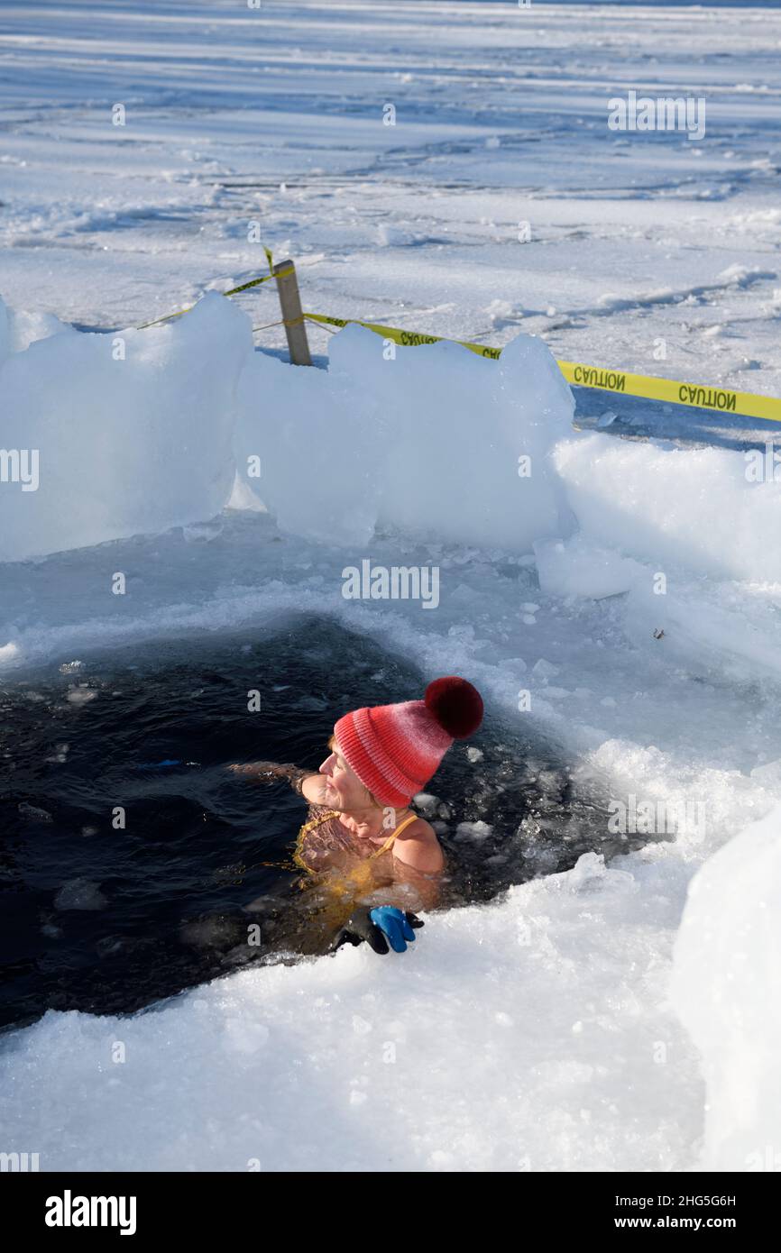 Femme avec chapeau et soleil du soir sur le visage dans un trou de glace pour une baignade en eau froide en hiver au lac Kempenfelt Bay Simcoe Barrie Ontario Banque D'Images