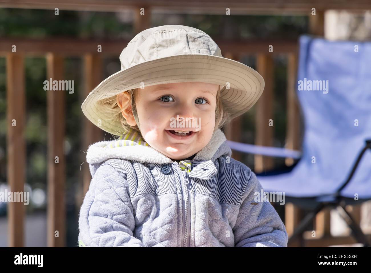 Portrait en gros plan d'un adorable garçon de trois ans souriant, lors d'une journée d'hiver lumineuse, portant un chapeau seau à visière et une veste épaisse et chaude avec un arrière-plan flou. Banque D'Images