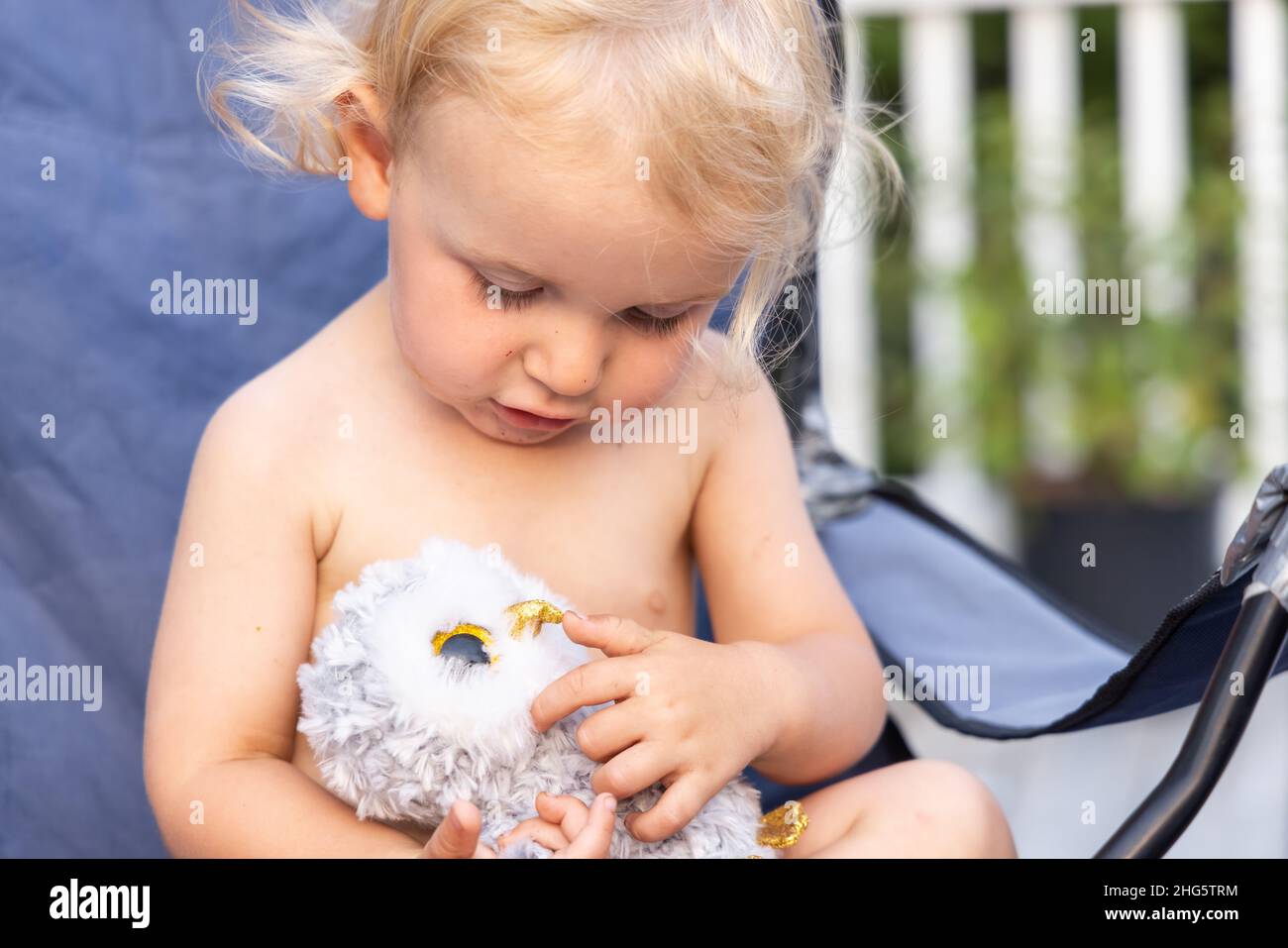 Gros plan sur un joli petit enfant d'âge préscolaire qui remplit le cadre, qui s'assoit à l'extérieur et qui regarde vers le bas et câlin un jouet en peluche. Banque D'Images