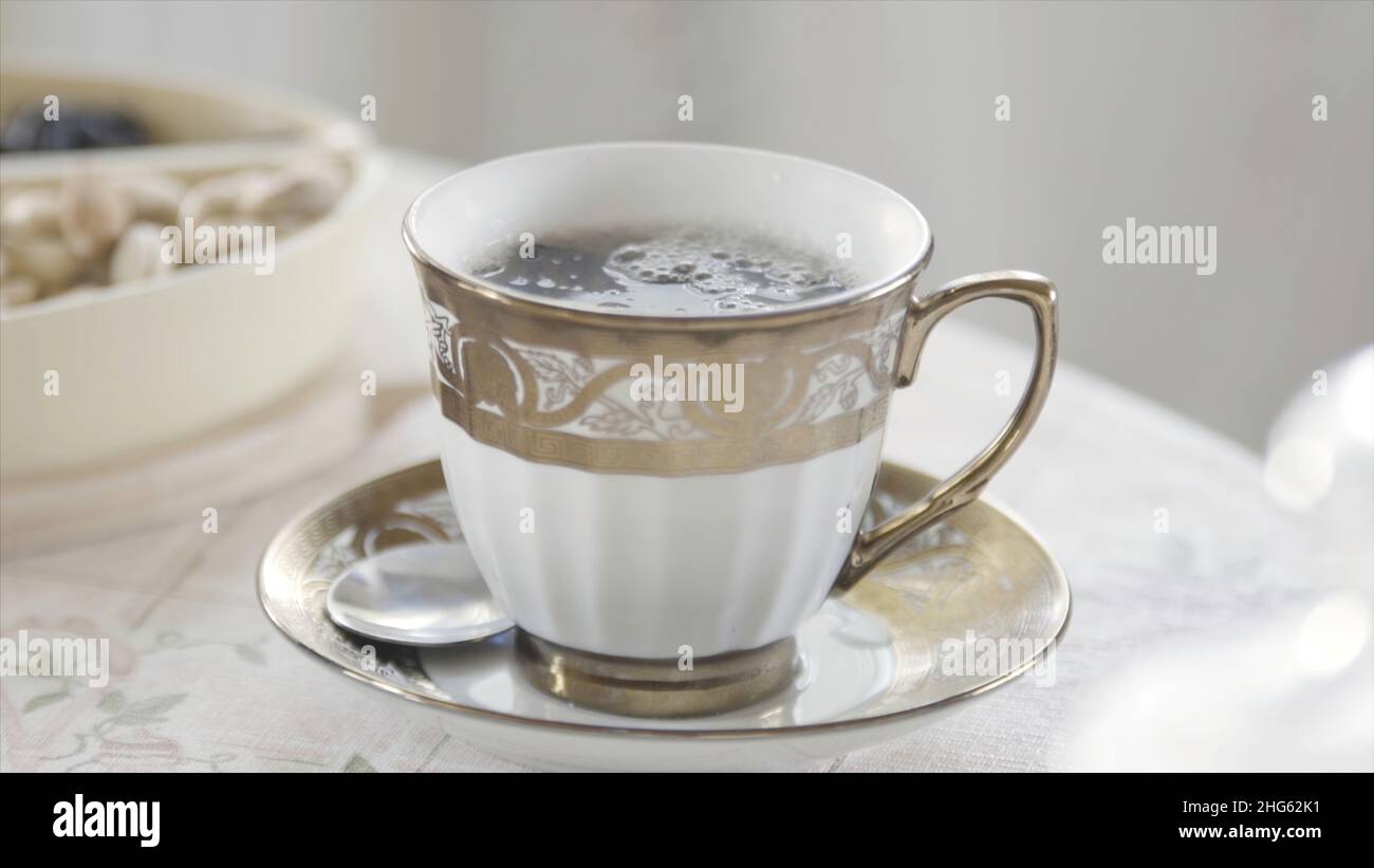 Gros plan d'une élégante tasse de thé chaud en porcelaine avec de la vapeur sur la table dans une pièce lumineuse.Petit déjeuner aristocratique le matin. Banque D'Images