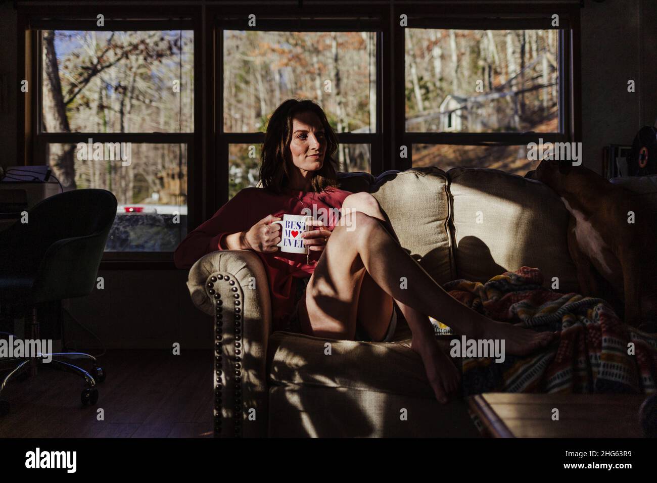 Une femme assise sur un canapé boit dans une tasse de café, meilleure maman. Banque D'Images