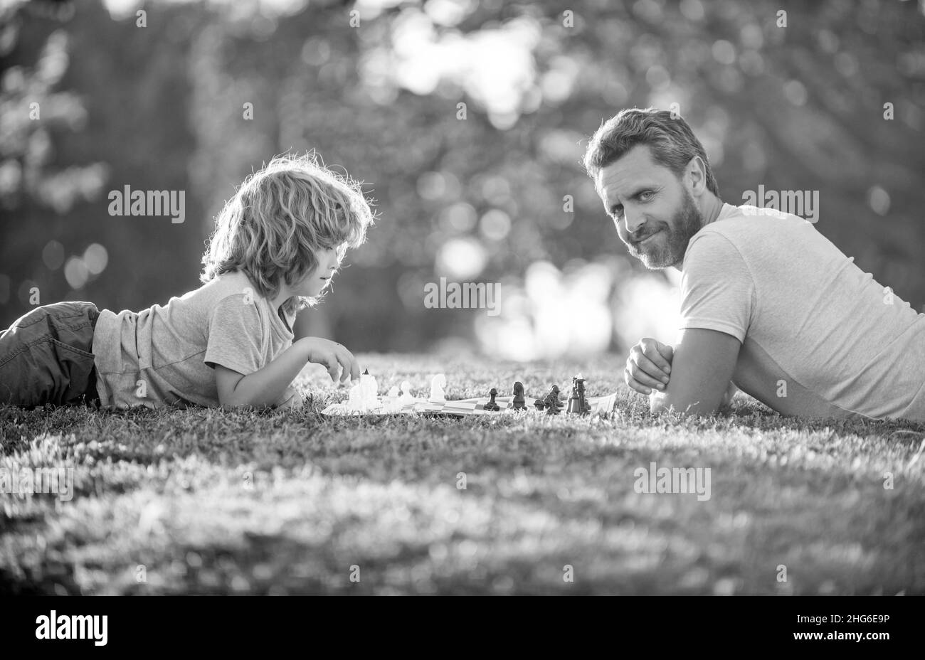 famille heureuse de père homme et fils garçon jouant aux échecs sur l'herbe verte dans le parc en plein air, sport logique Banque D'Images