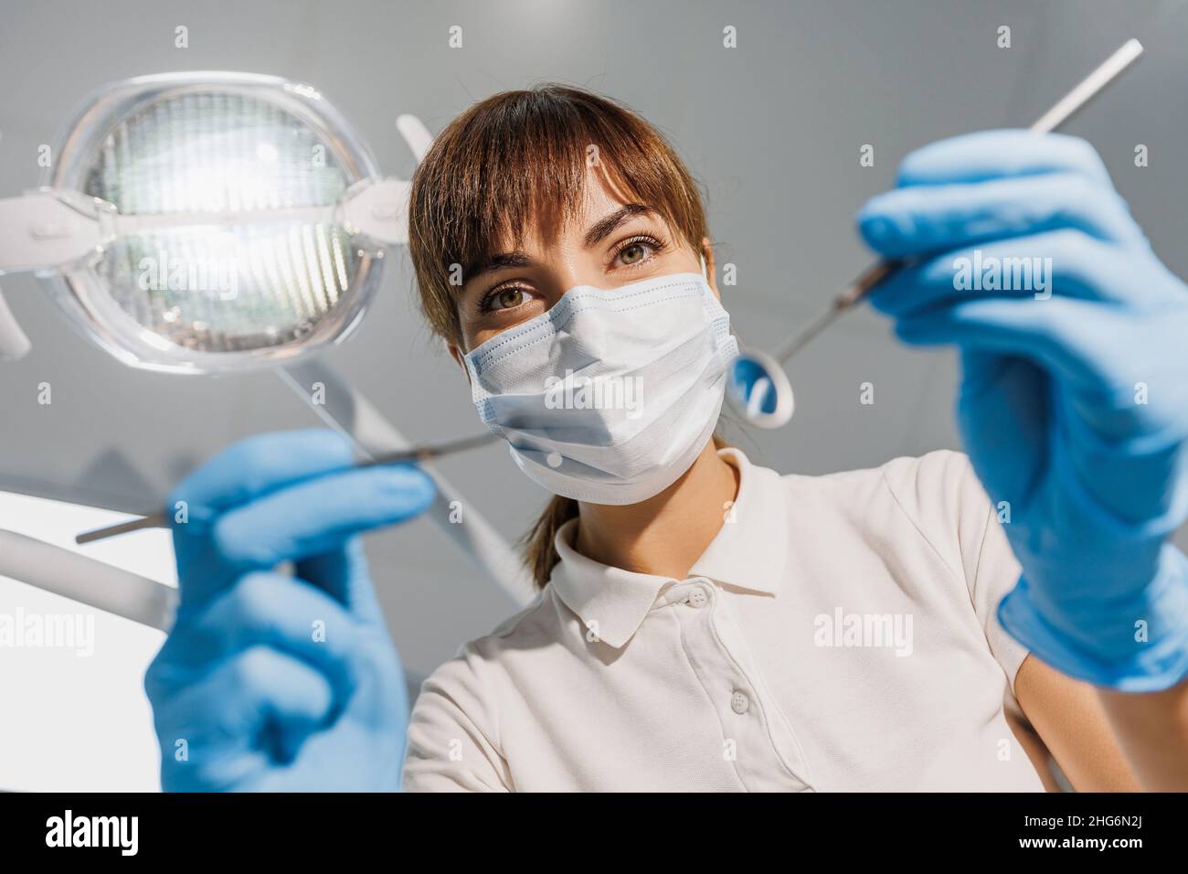 Femme dentiste dans le masque bleu et les gants examinent les dents avec la sonde et le miroir.Vue du siège du patient au médecin.Photo créative sur le thème dentaire.Concept de la procédure de traitement dentaire en clinique. Banque D'Images