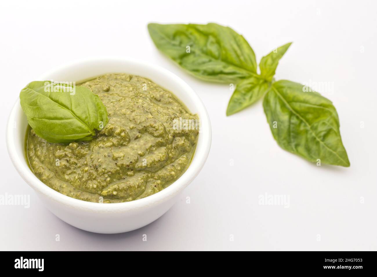 Un gros plan d'un bol de pesto maison et d'une feuille de basilic. Banque D'Images