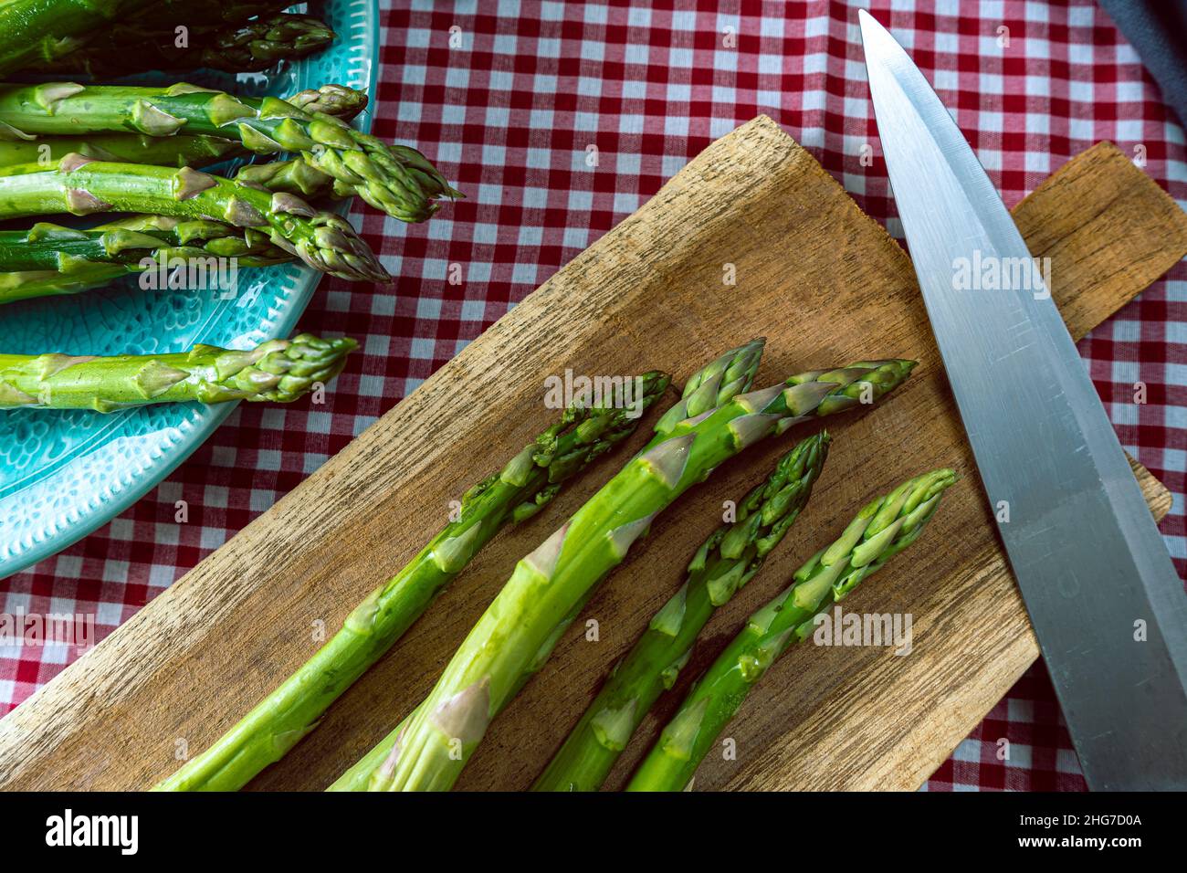 Un groupe d'asperges vertes sur une planche à découper en bois à côté d'un couteau sur une table avec une nappe à carreaux. Vue en hauteur, Banque D'Images