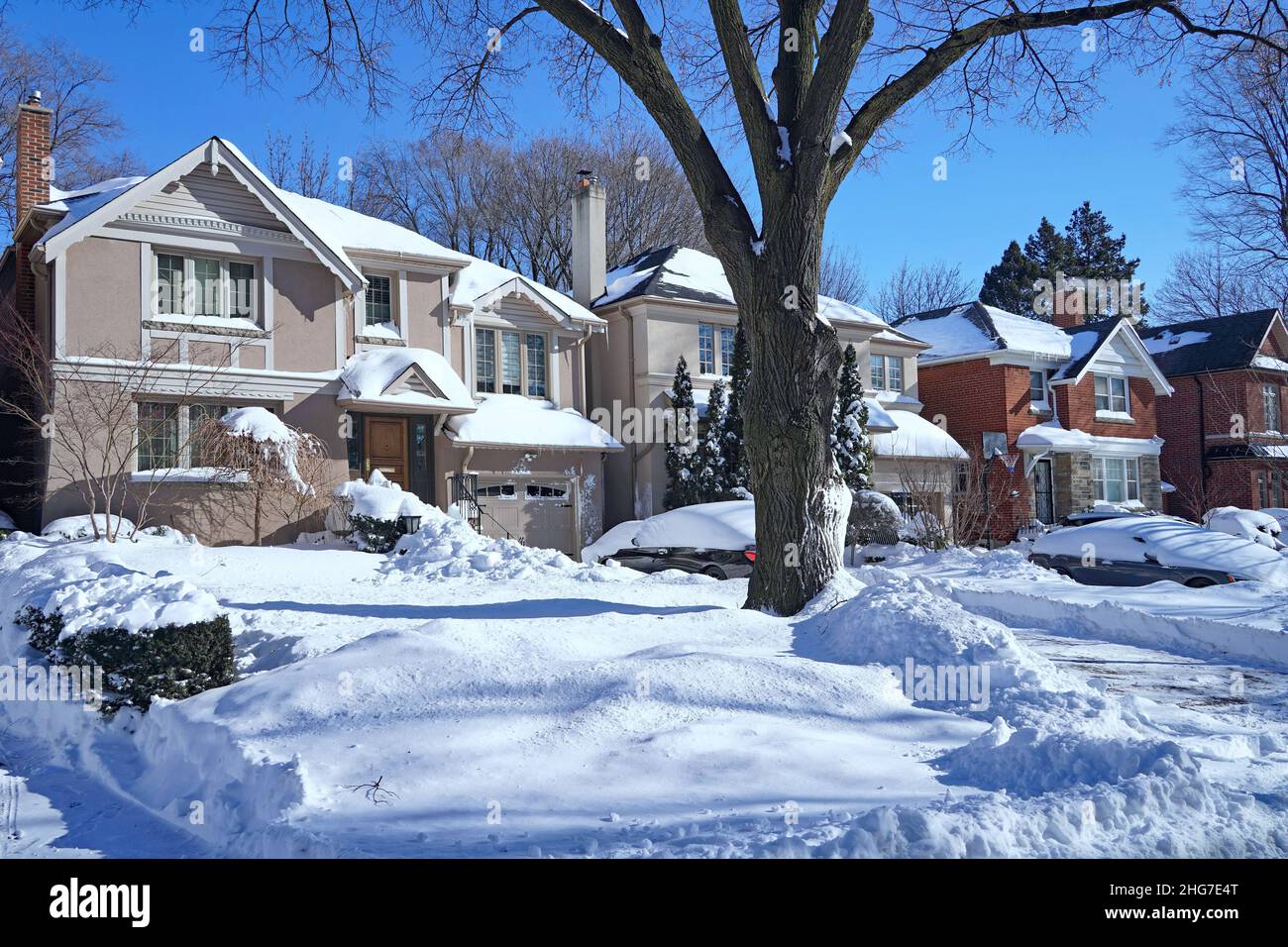 Une rue résidentielle de banlieue lors d'une journée d'hiver ensoleillée après une grosse chute de neige, avec des voitures dans l'allée enfouie dans la neige Banque D'Images