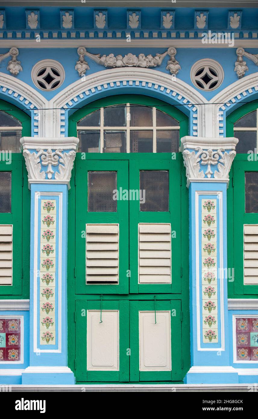 Vue rapprochée de face d'un atelier Peranakan d'avant-guerre à Singapour, présentant des fenêtres cintrées complexes, des volets en bois anciens et des carreaux. Banque D'Images