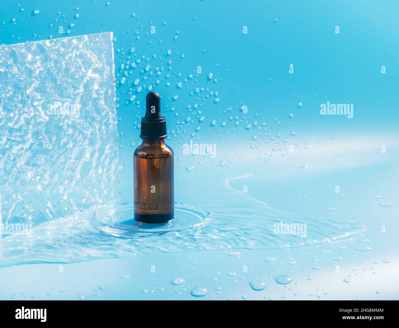 Une bouteille avec une pipette, un produit cosmétique, des éclaboussures et des gouttes d'eau sur fond bleu Banque D'Images