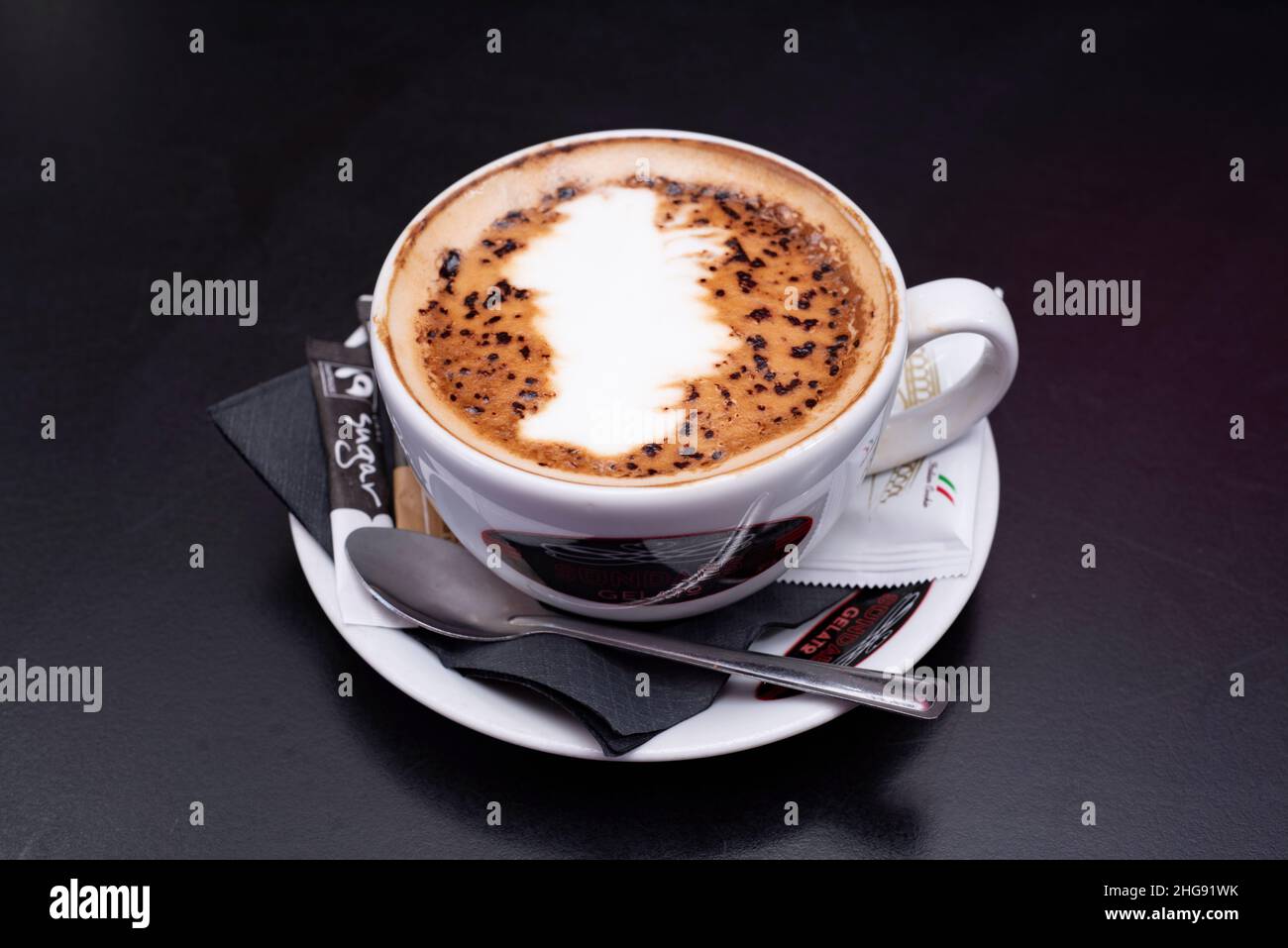 Café – un cappuccino au chocolat servi dans une tasse de thé avec soucoupe, sachet de sucre et cuillère à thé Banque D'Images