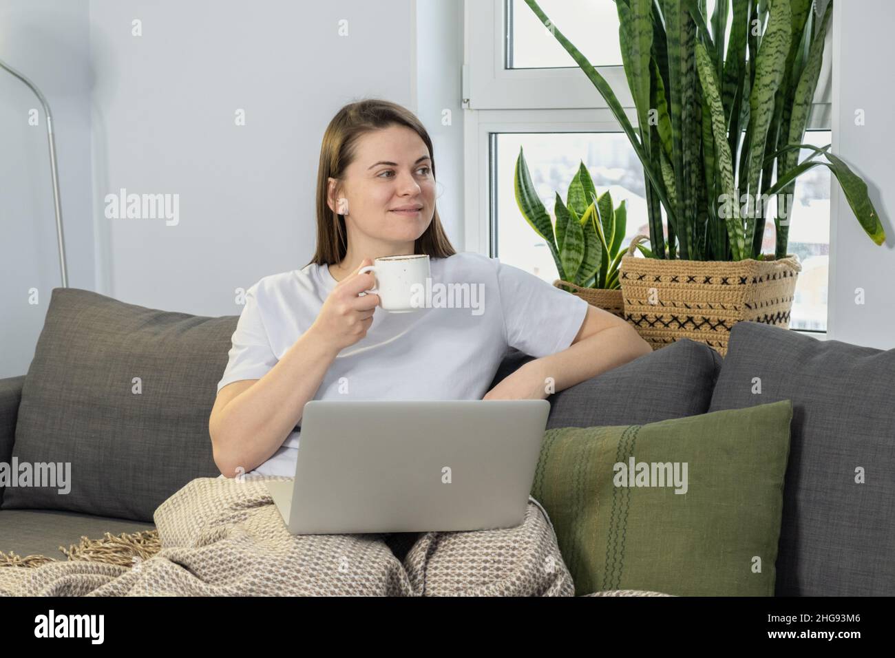 Jeune femme avec mug utilisant un ordinateur portable se détendre à la maison le week-end Banque D'Images