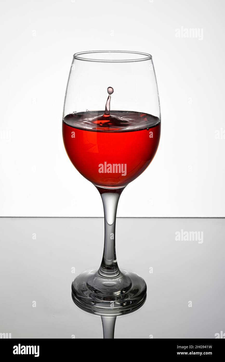 Verre de vin rouge, sur une surface réfléchissante avec un fond blanc. Banque D'Images