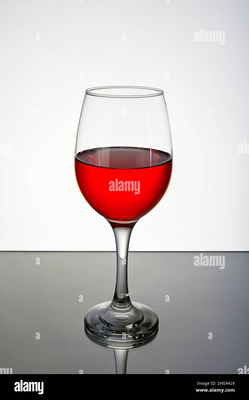 Verre de vin rouge, sur une surface réfléchissante avec un fond blanc. Banque D'Images