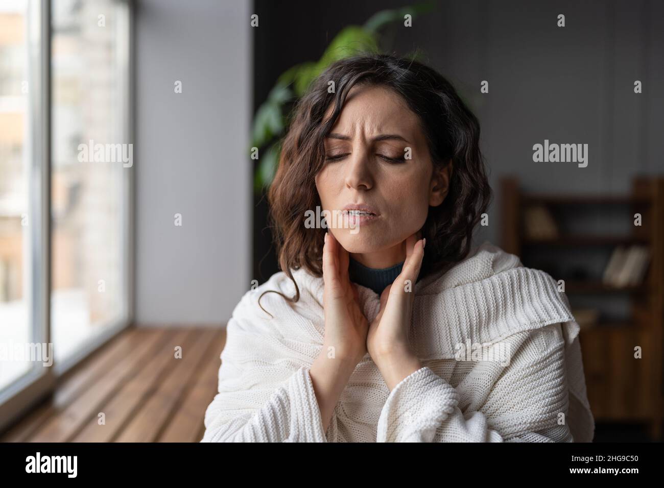 Bouleversée malade femme debout à la maison touchant des glandes gonflées, souffrant d'angine ou d'amygdalite Banque D'Images