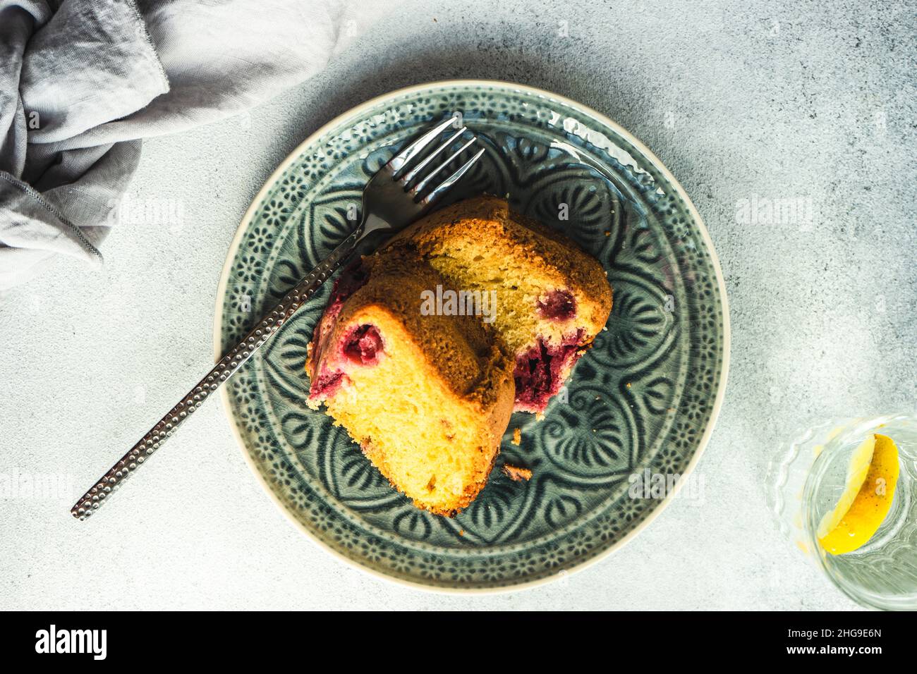 Tranche de gâteau éponge de myrtille et de cerise sur une assiette avec un verre d'eau de citron Banque D'Images