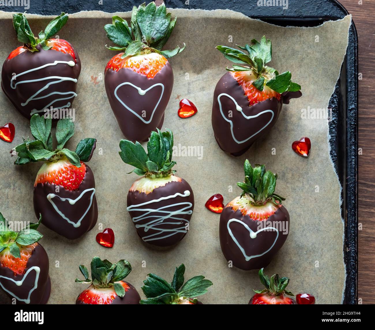 Fraises enrobées de chocolat décorées sur papier parchemin pour la Saint-Valentin. Banque D'Images