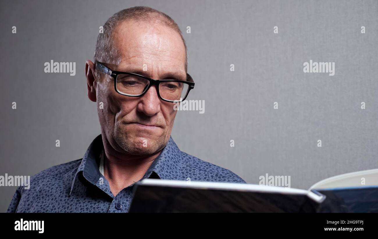 Homme senior dans des lunettes élégantes lit le livre sur fond gris Banque D'Images
