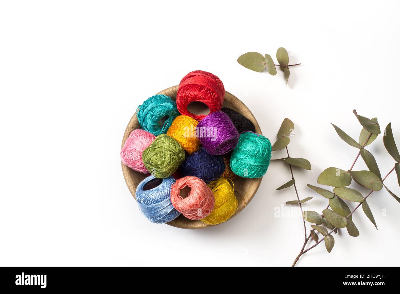 Bobines de fil de couleur dans un bol en bois sur fond blanc avec des leves d'eucalyptus Banque D'Images