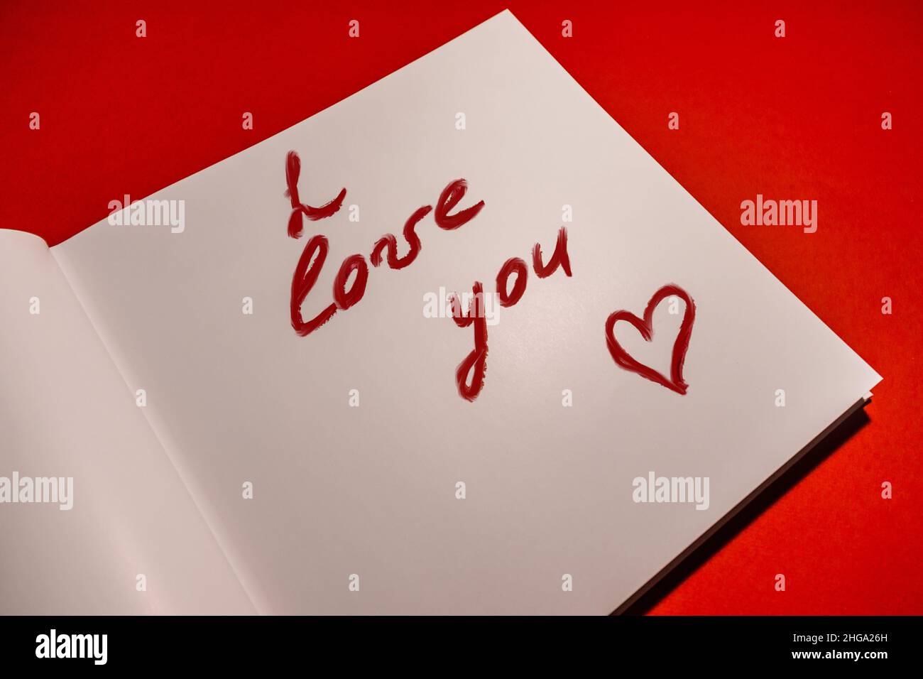 Une déclaration d'amour est écrite en rouge à lèvres sur papier sur fond rouge. Banque D'Images