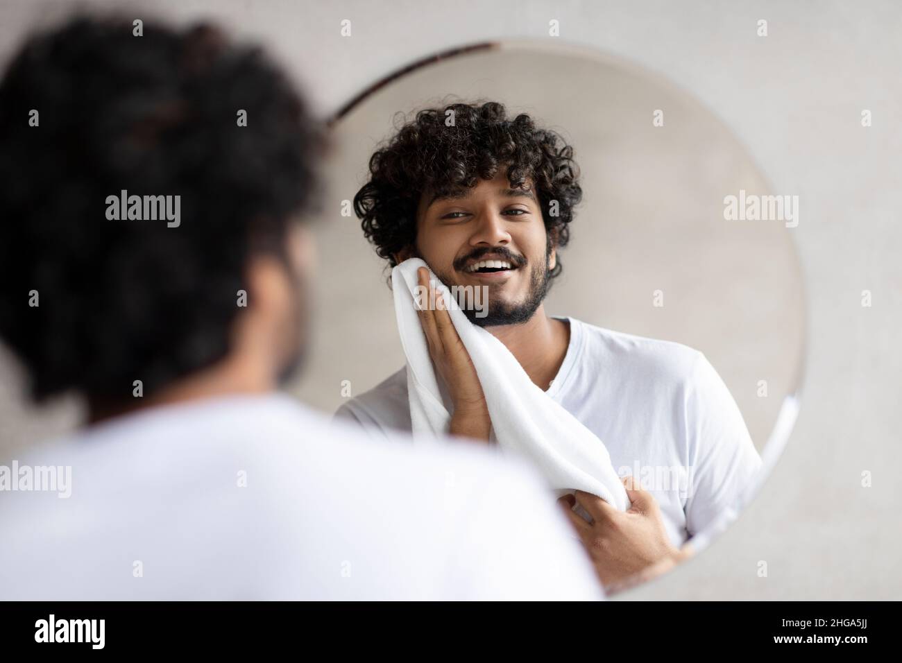 Concept de routine quotidienne.Un Indien excité essuyant son visage avec une serviette en se tenant dans la salle de bains, regardant dans le miroir Banque D'Images