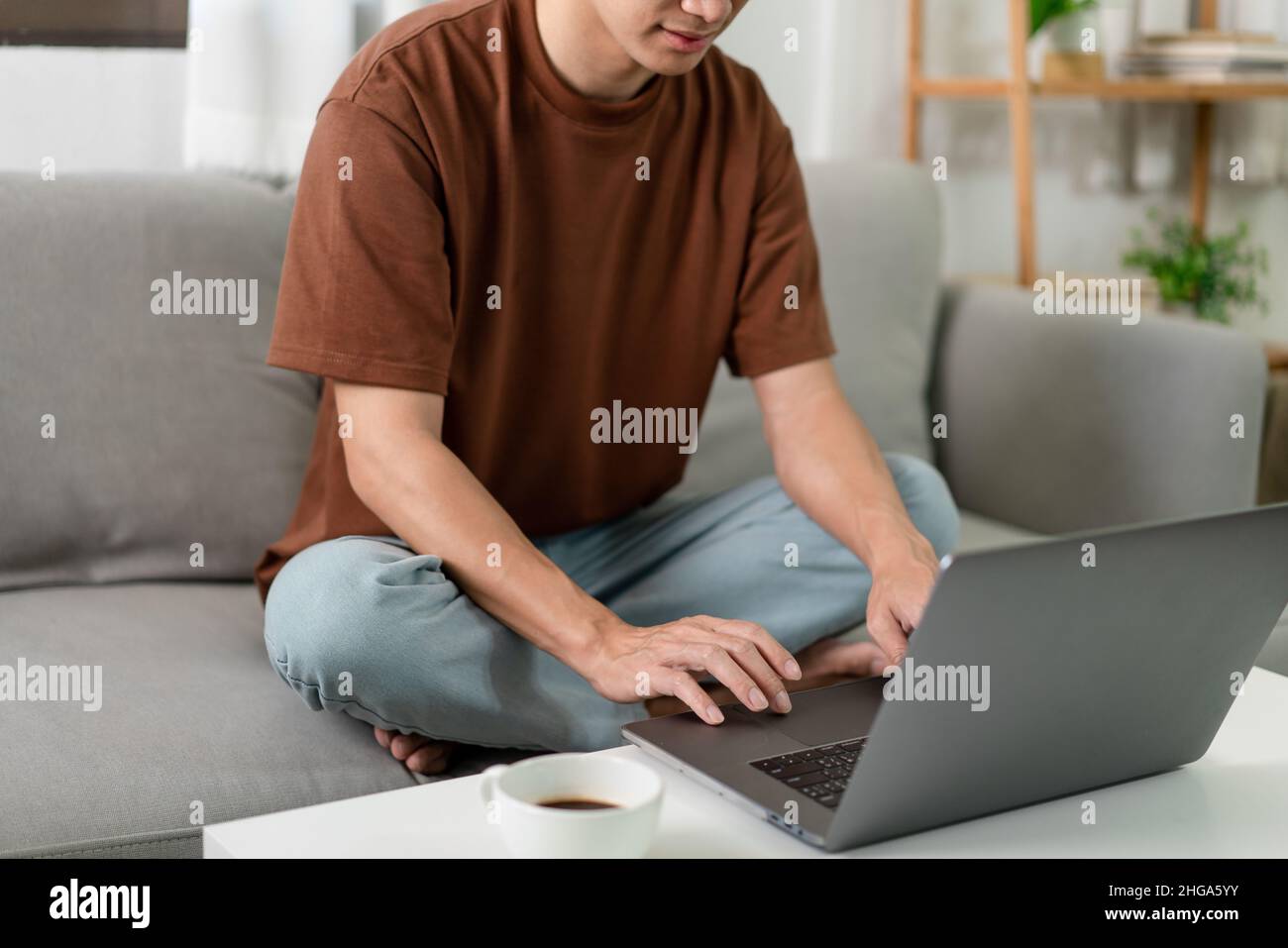 Concept de technologie l'homme en T-shirt marron se concentrant sur taper quelque chose sur son ordinateur portable. Banque D'Images