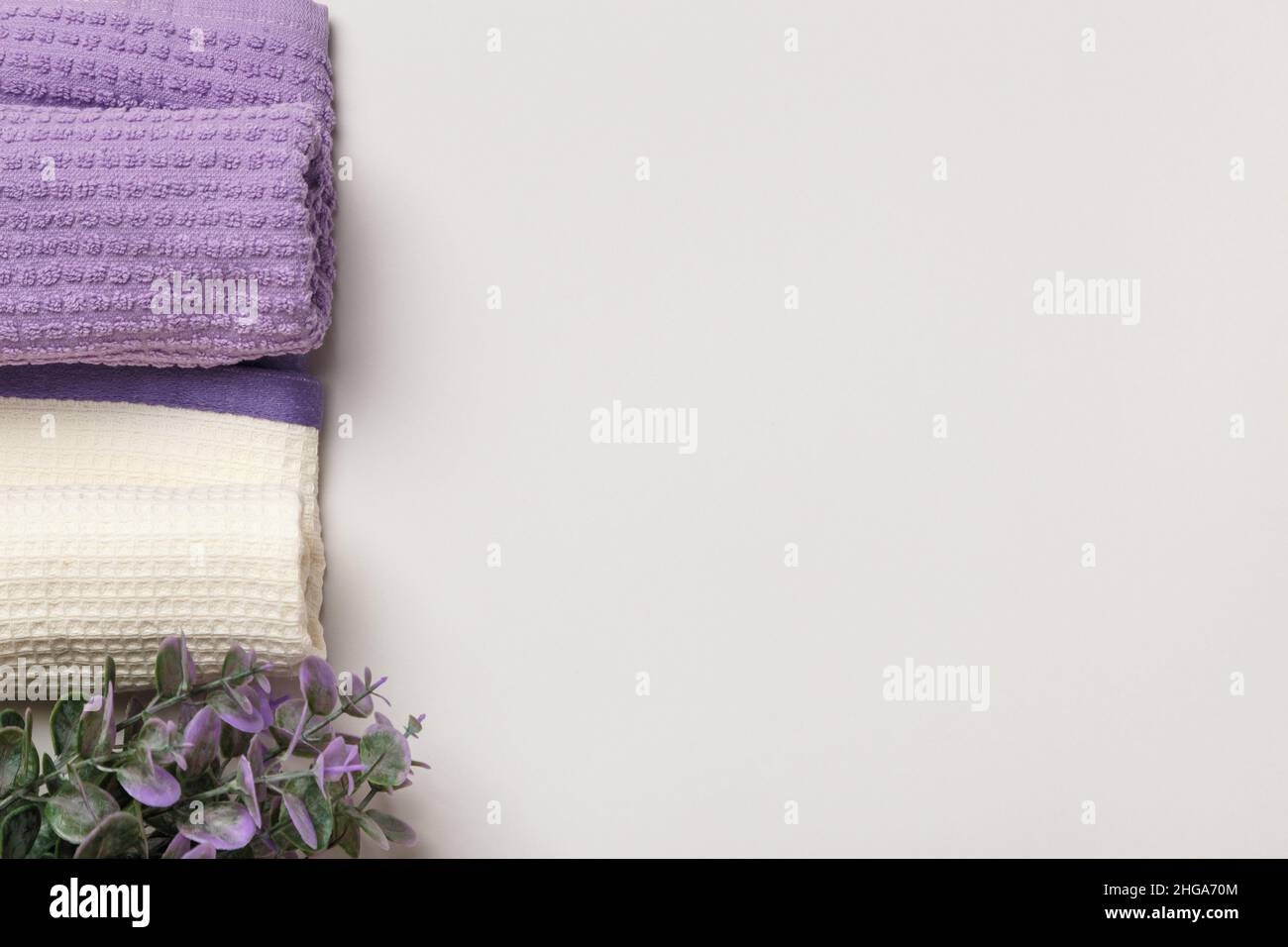 Serviettes gaufrée blanches et violettes enroulées et fleur sur fond gris. Banque D'Images
