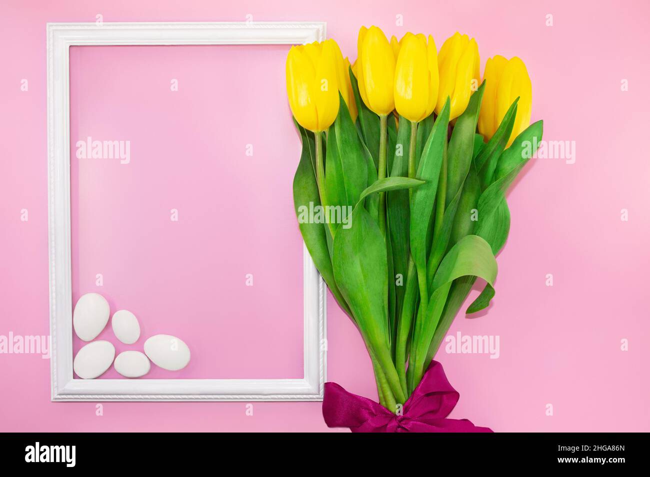 Bouquet de tulipes jaunes avec noeud avec cadre et pierres blanches sur fond rose.Vacances, anniversaire, 8 mars, Fête des mères, Journée internationale de la femme.COP Banque D'Images