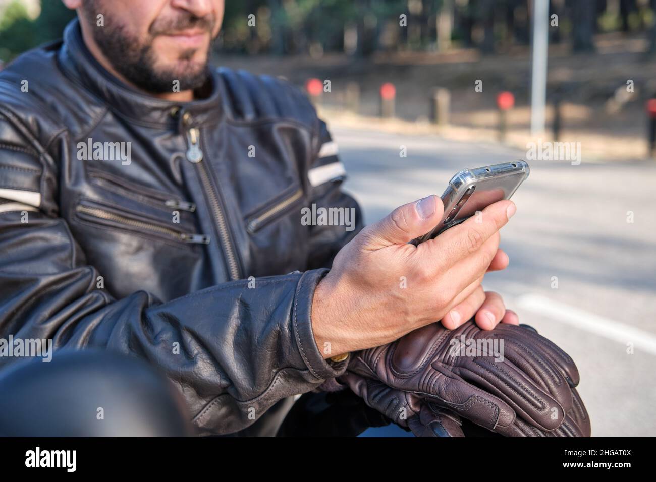 Un motard élégant utilisant un téléphone portable sur une route rurale. Banque D'Images