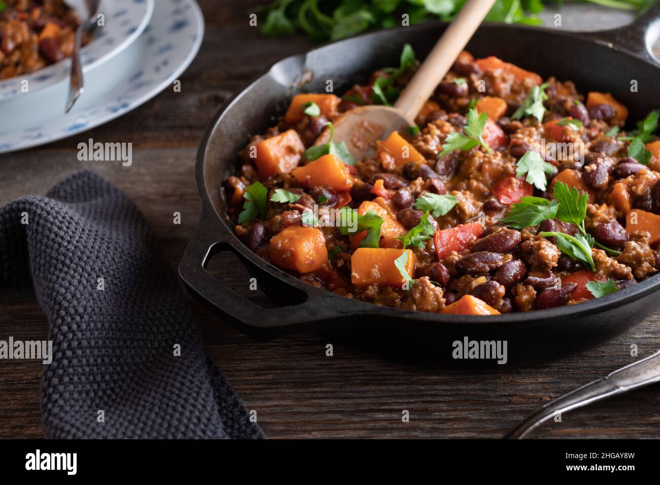 Ragoût de haricots avec du bœuf haché, des patates douces et des légumes servis dans une poêle rustique en fonte sur une table en bois. Repas sain et sans gluten Banque D'Images
