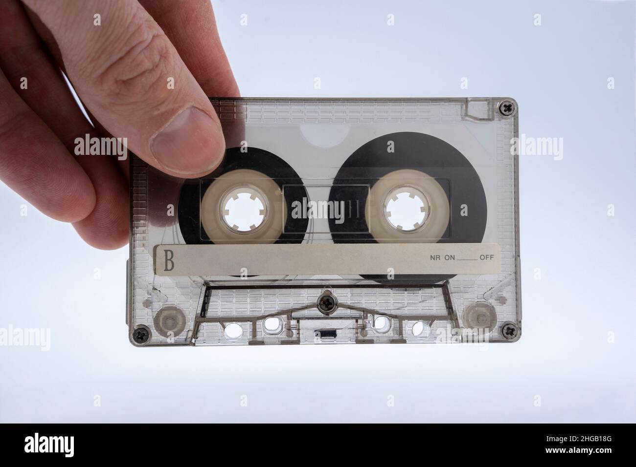 La main d'un homme tient une cassette audio transparente en vitrail pour un magnétophone sur fond blanc gros plan, le film magnétique est visible à travers Banque D'Images