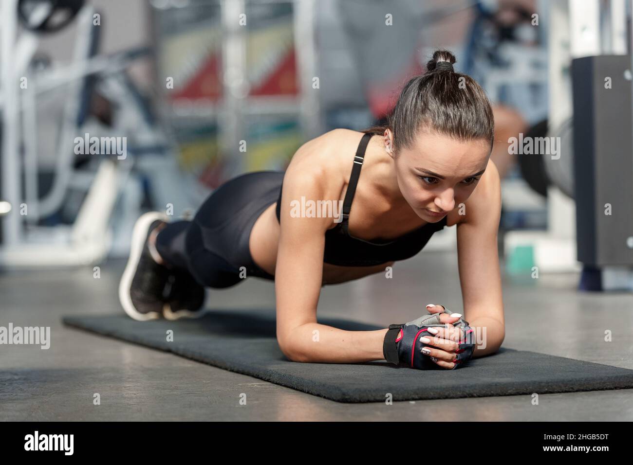 Jeune femme sportive dans un vêtement de sport noir faisant de l'exercice de planche sur un tapis dans la salle de gym Banque D'Images