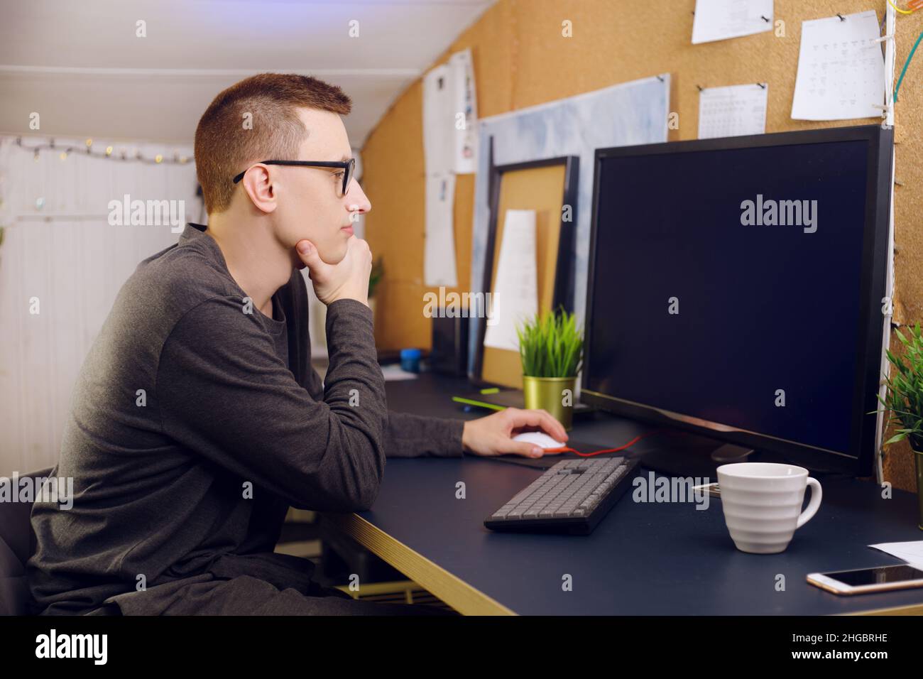 L'homme en lunettes utilise le clavier et la souris regarde l'écran vert.Un homme travaille à la maison.Restez à la maison, indépendant, joueur. Banque D'Images