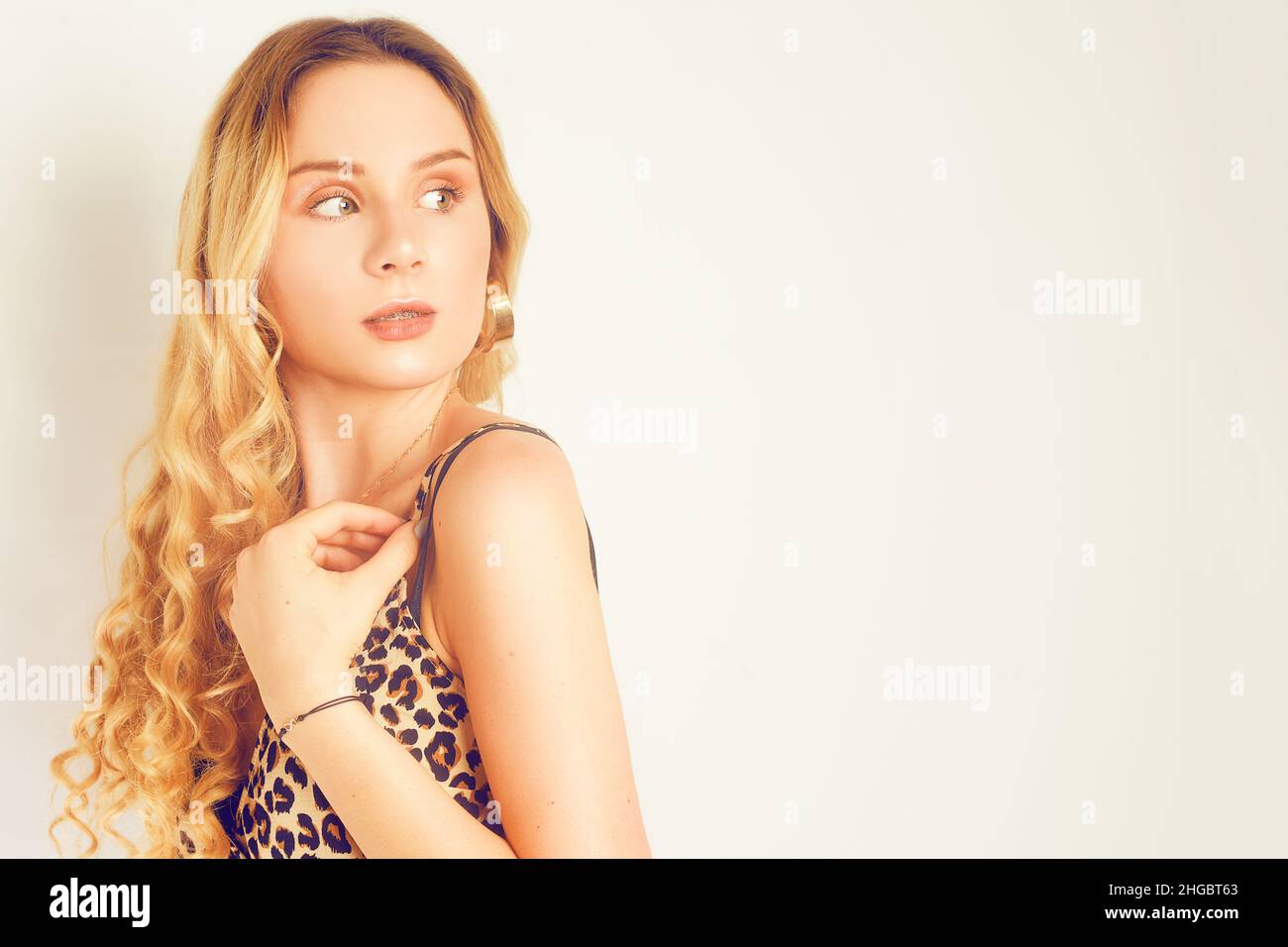 Portrait d'une belle blonde aux cheveux longs.Fille avec boucles d'oreilles dorées, bijoux fantaisie, robe avec imprimé léopard.Jeune fille avec bretelles, assiette, perf Banque D'Images