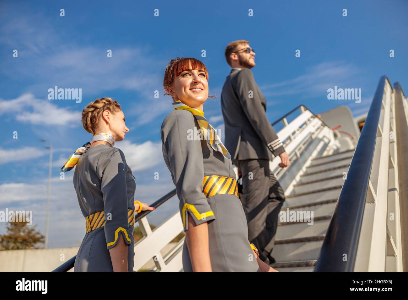 Deux hôtesses et un pilote d'aviation grimpent les escaliers d'embarquement en avion sous un ciel bleu Banque D'Images