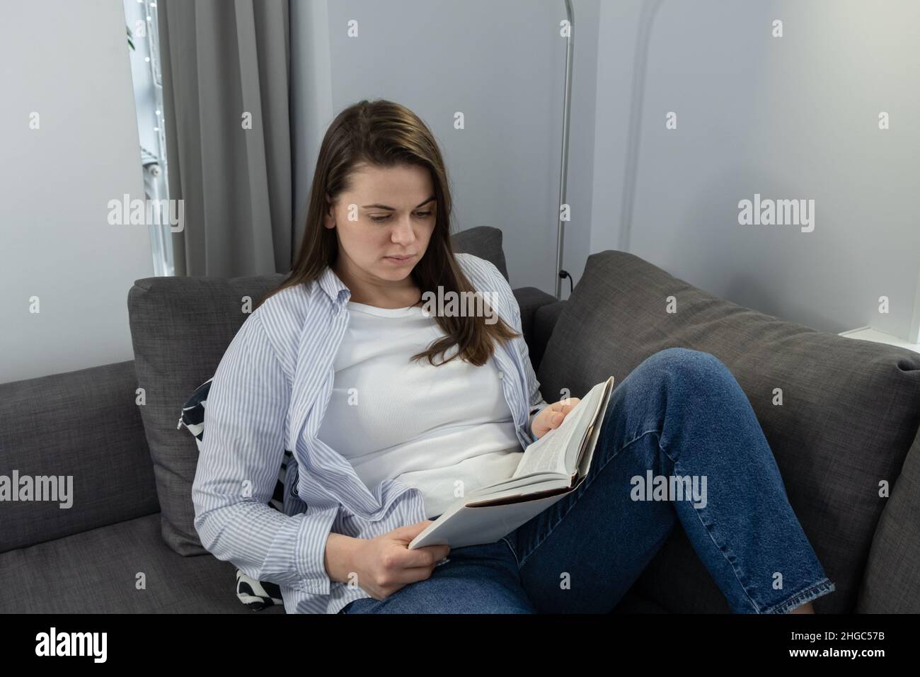 Femme sur un canapé à la maison avec un livre sur sa poitrine, prenant une pause, regardant sa montre intelligente.Concept de fatigue et de troubles du sommeil Banque D'Images