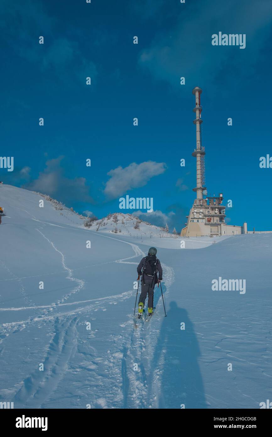 Personne ski en montée avec une grande antenne de télévision et radio en béton sur la piste de ski de Krvavec au soleil du soir. Banque D'Images