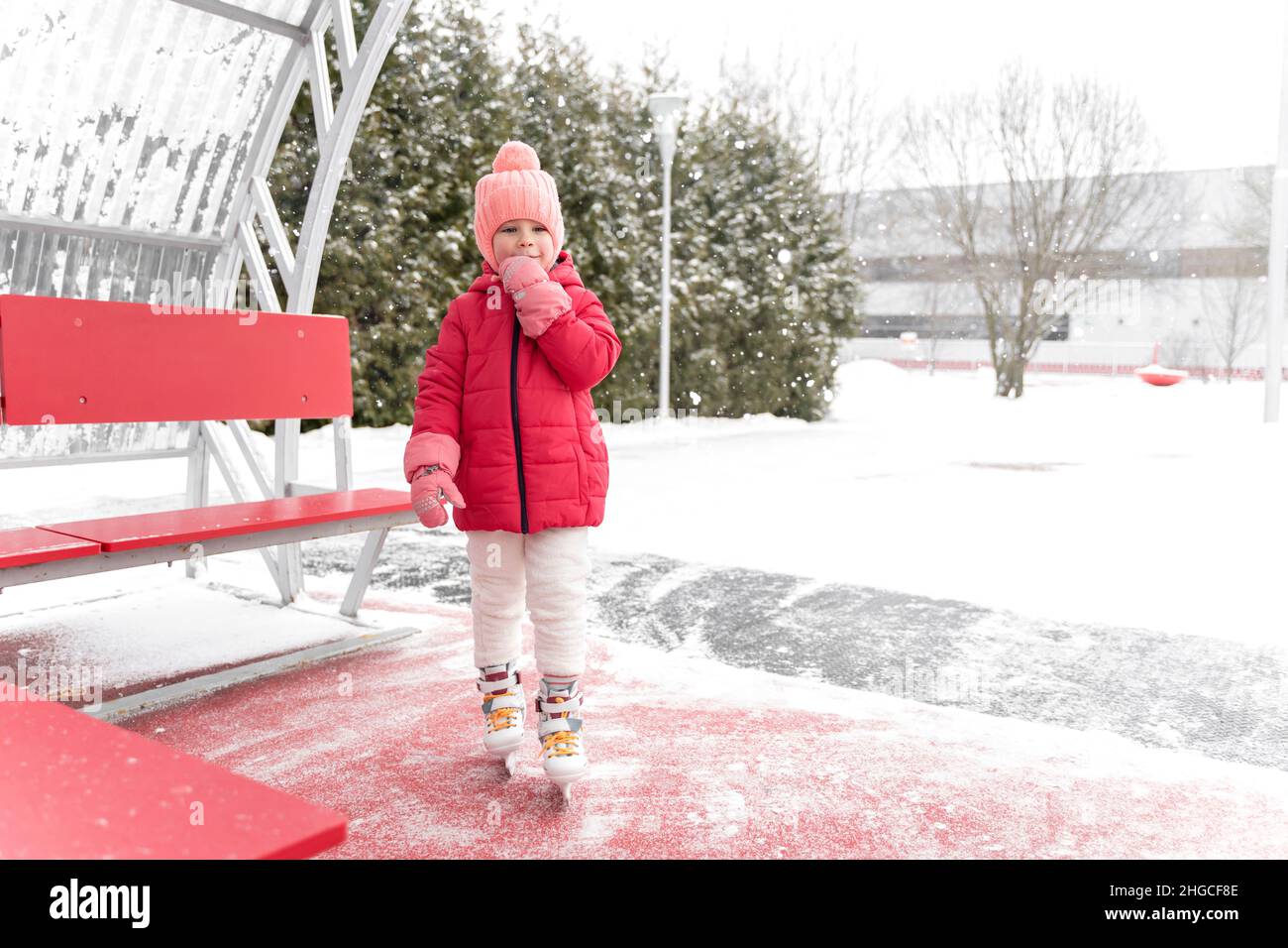 adorable petite fille dans une veste rouge et skates va skate sur la patinoire Banque D'Images