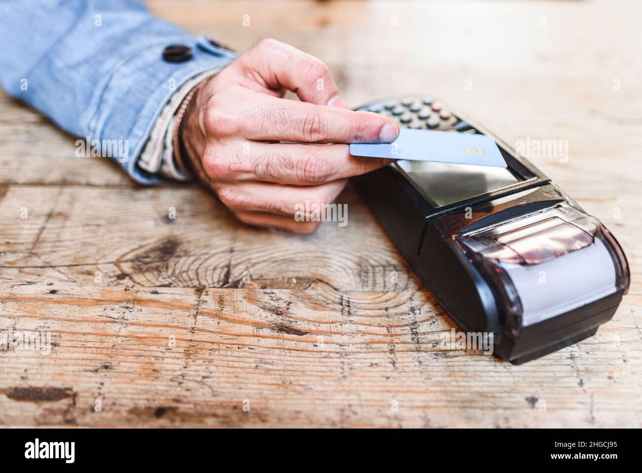 Grand angle de l'homme anonyme utilisant la carte de crédit et le terminal sans contact pour payer la commande sur table en bois dans le restaurant Banque D'Images