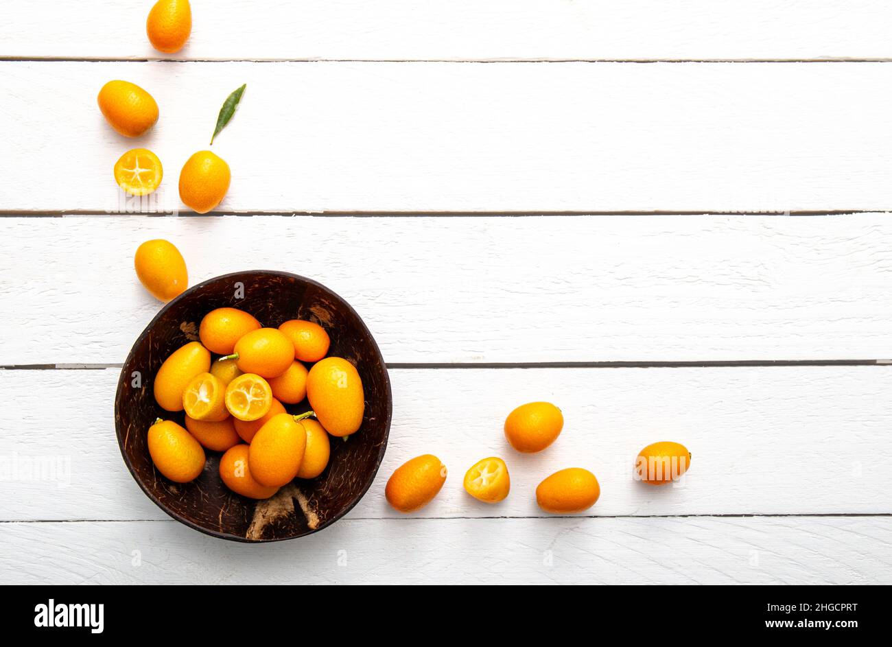 Kumquats ou cumquats ( Citrus japonica) à l'intérieur d'un bol de noix de coco et sur fond de bois blanc.Concept de bordure de cadre alimentaire aux agrumes. Banque D'Images