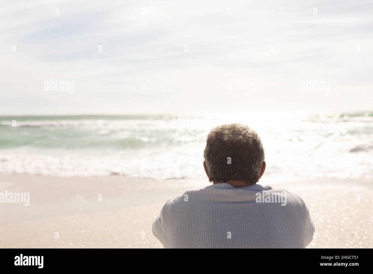 Vue arrière de l'homme biracial à la retraite regardant l'horizon sur la mer par jour ensoleillé depuis la plage Banque D'Images