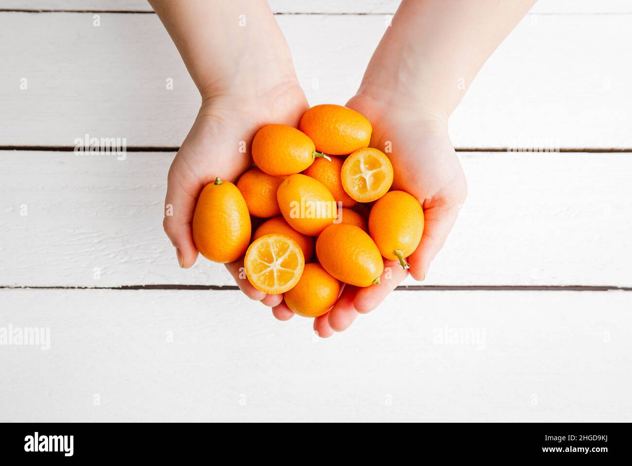 Au-dessus de la vue des mains d'enfants tenant des kumquats ou des cumquats ( Citrus japonica) sur fond de bois blanc.Concept de bordure de cadre alimentaire d'agrumes sains. Banque D'Images